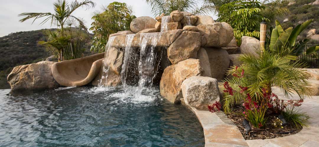 beige waterslide with rock waterfall and tropical landscaping
