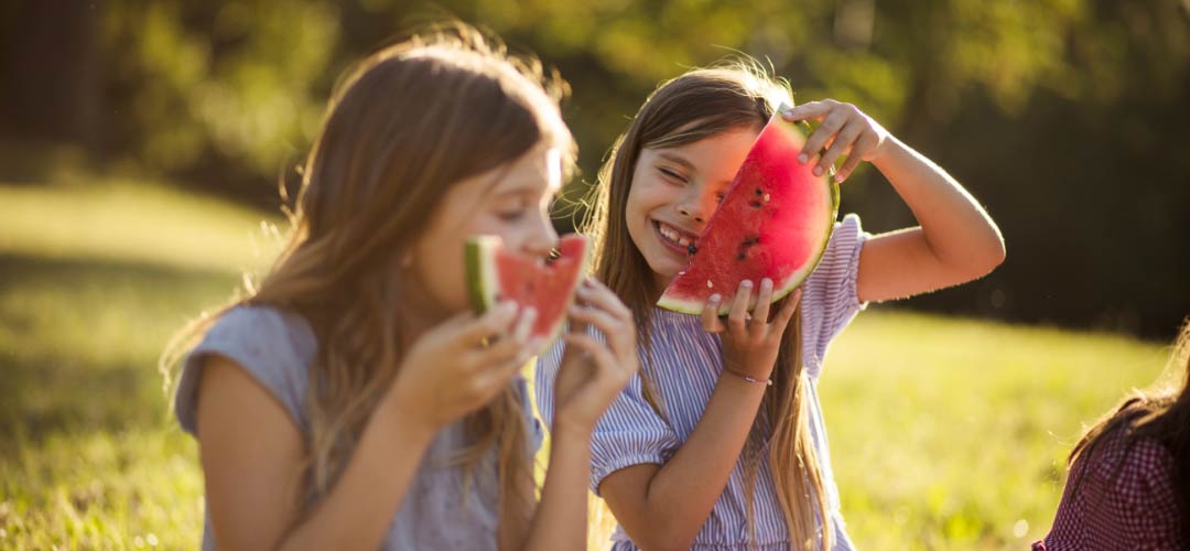 Two Girls Enjoying Slices of Watermelon in Backyard During Summer
